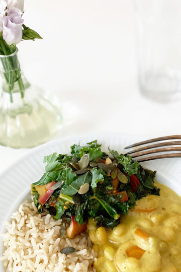 Ett fat med vegansk currygryta, ris och lättfräst grönkål står bredvid en vas med blommor.