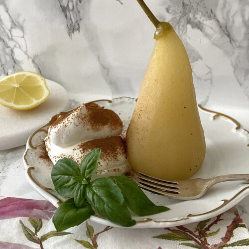 Inkokta päron med ingefära, grädde och kanel på ett fat med en gaffel.
